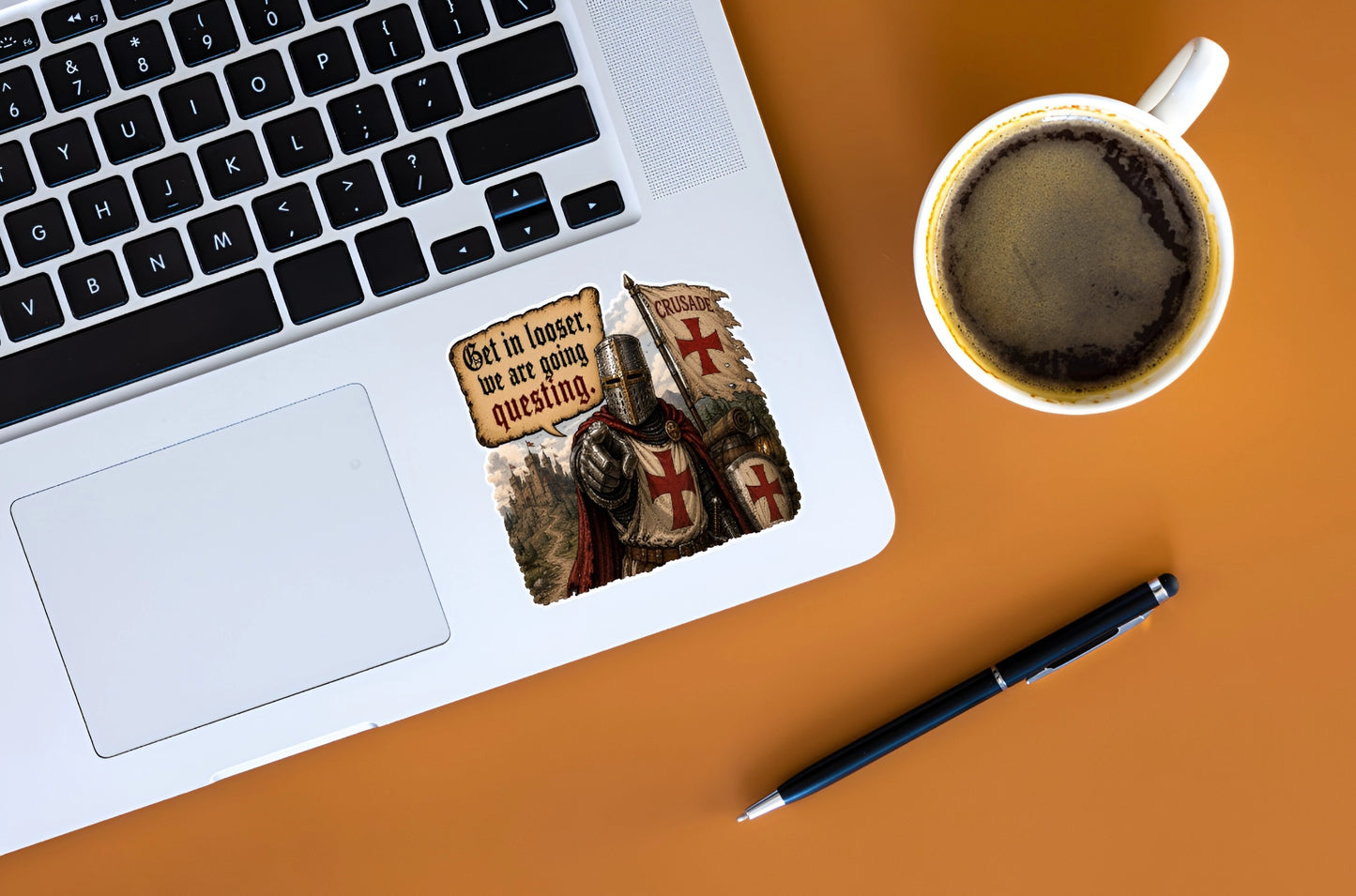 Funny Going Questing medieval knight sticker displayed on a silver laptop beside coffee
