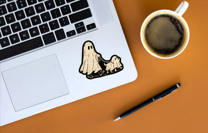 Vintage Halloween ghost and ghost dog sticker displayed on a silver laptop beside coffee