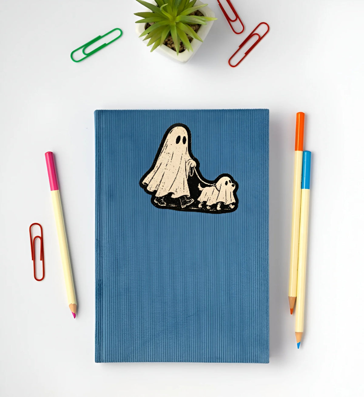 Vintage ghost walking a ghost dog Halloween sticker displayed on a blue notebook