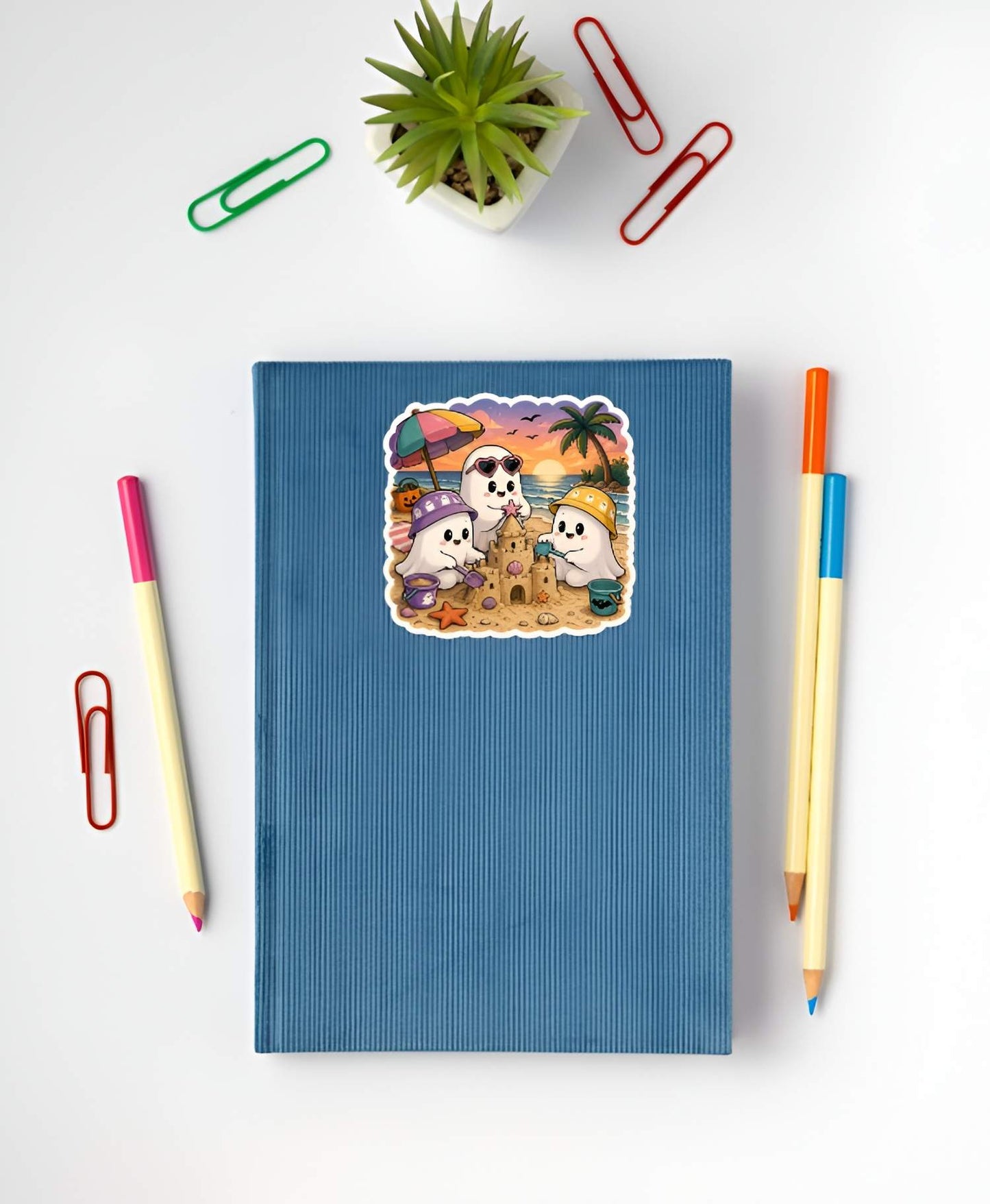 Blue notebook with a beach-themed sticker featuring cartoon characters on a white background with stationery items.
