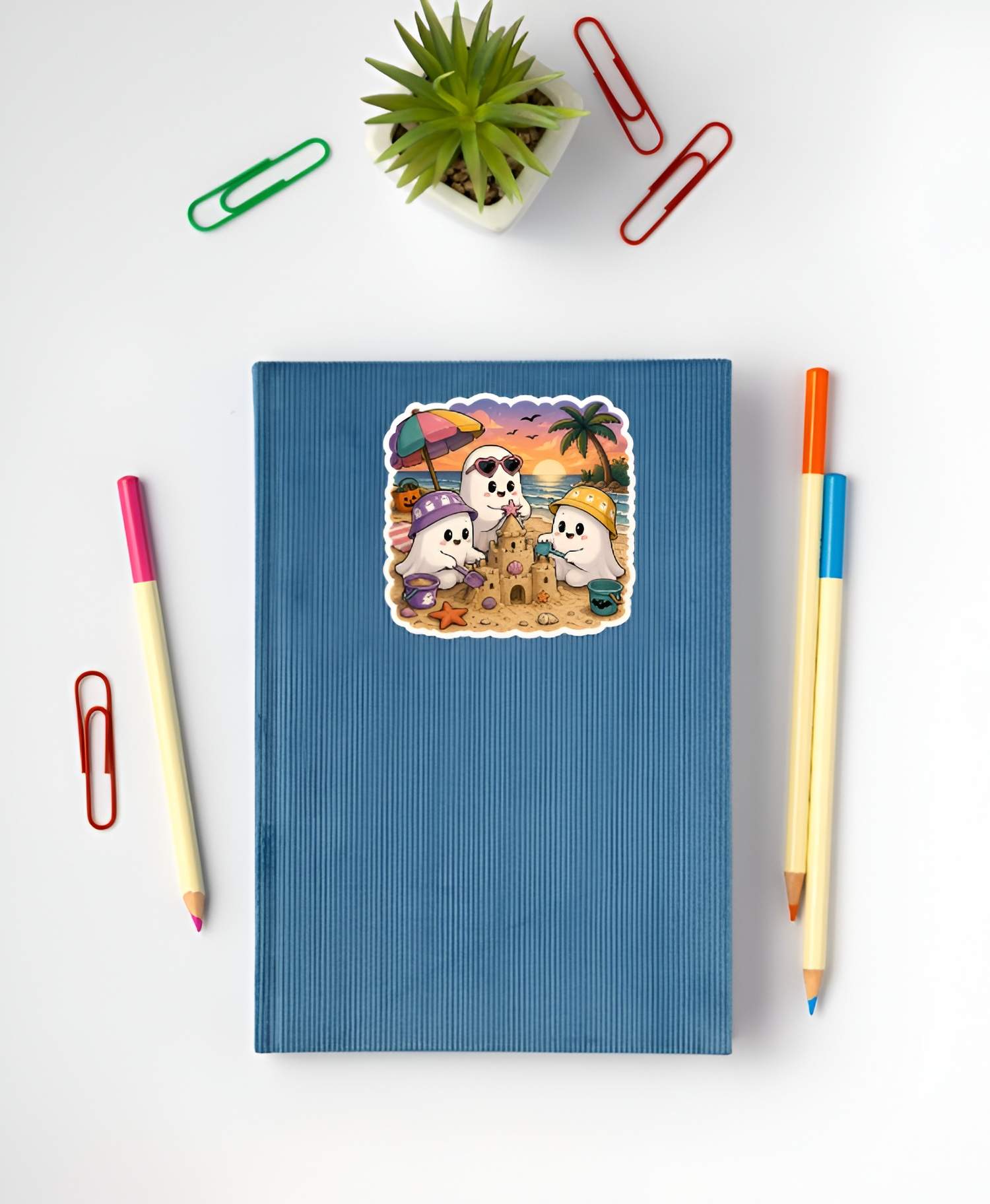 Blue notebook with a beach-themed sticker featuring cartoon characters on a white background with stationery items.