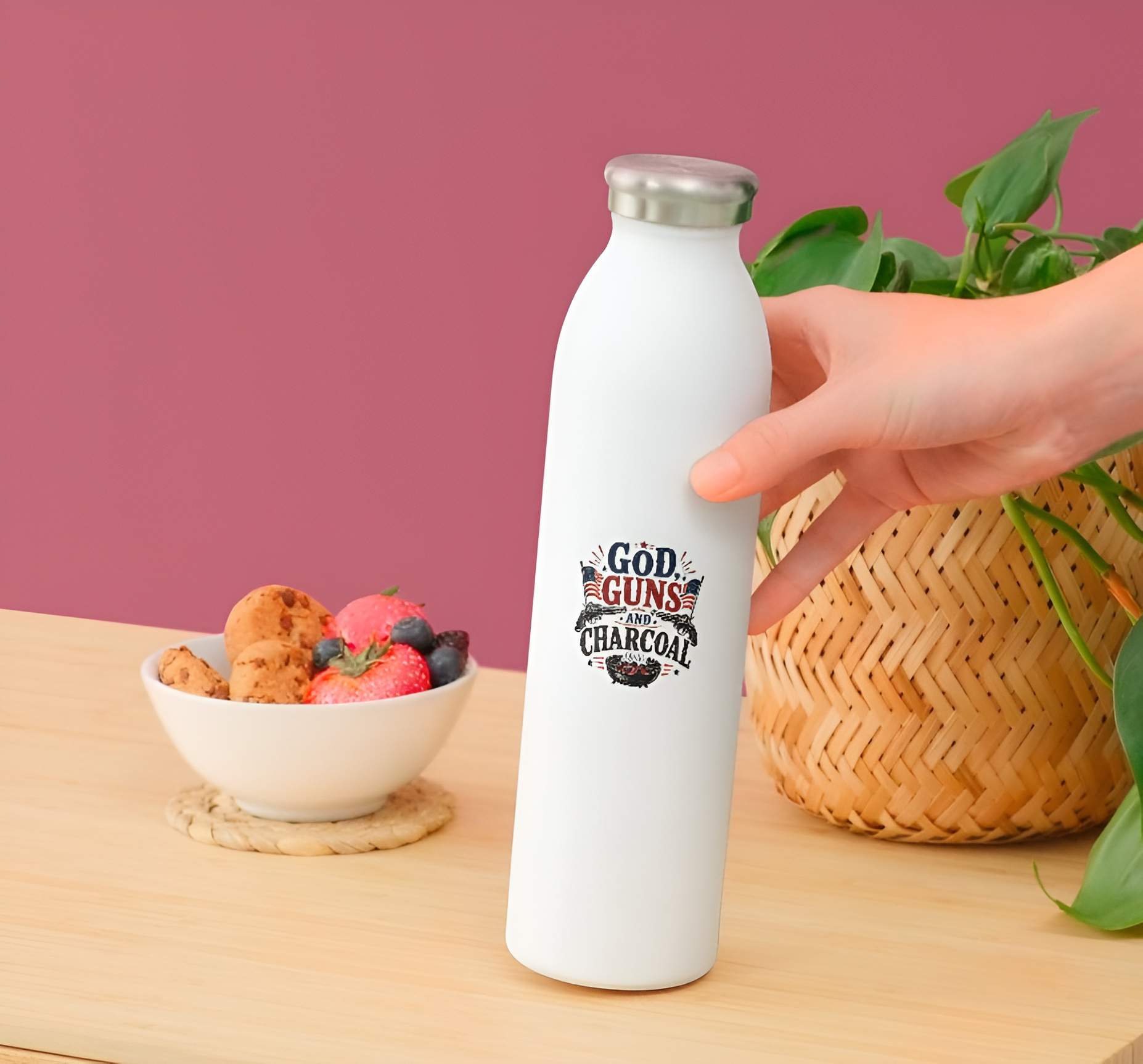 White water bottle with a printed design held by a hand on a wooden table with a bowl of snacks and a plant in the background.