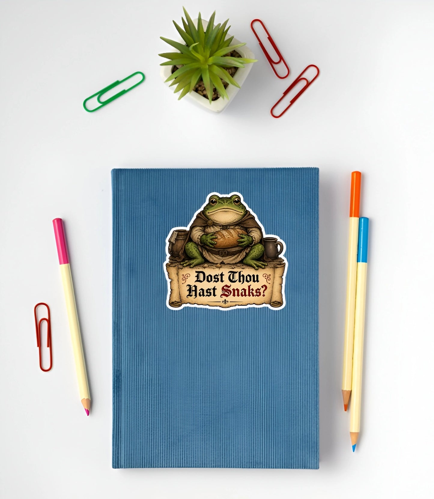 Funny Dost Thou Hast Snaks frog sticker displayed on a blue notebook.