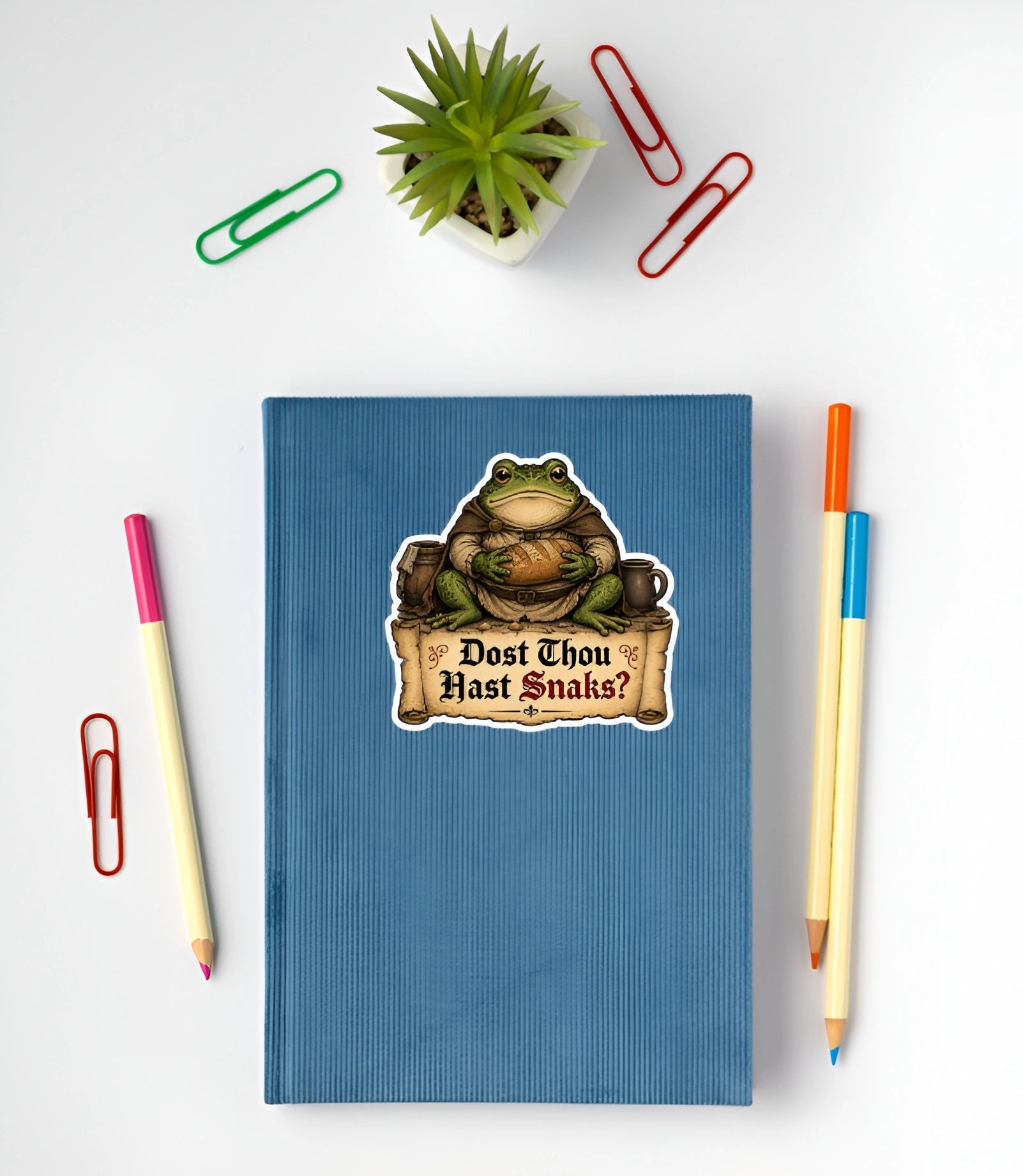 Funny Dost Thou Hast Snaks frog sticker displayed on a blue notebook.