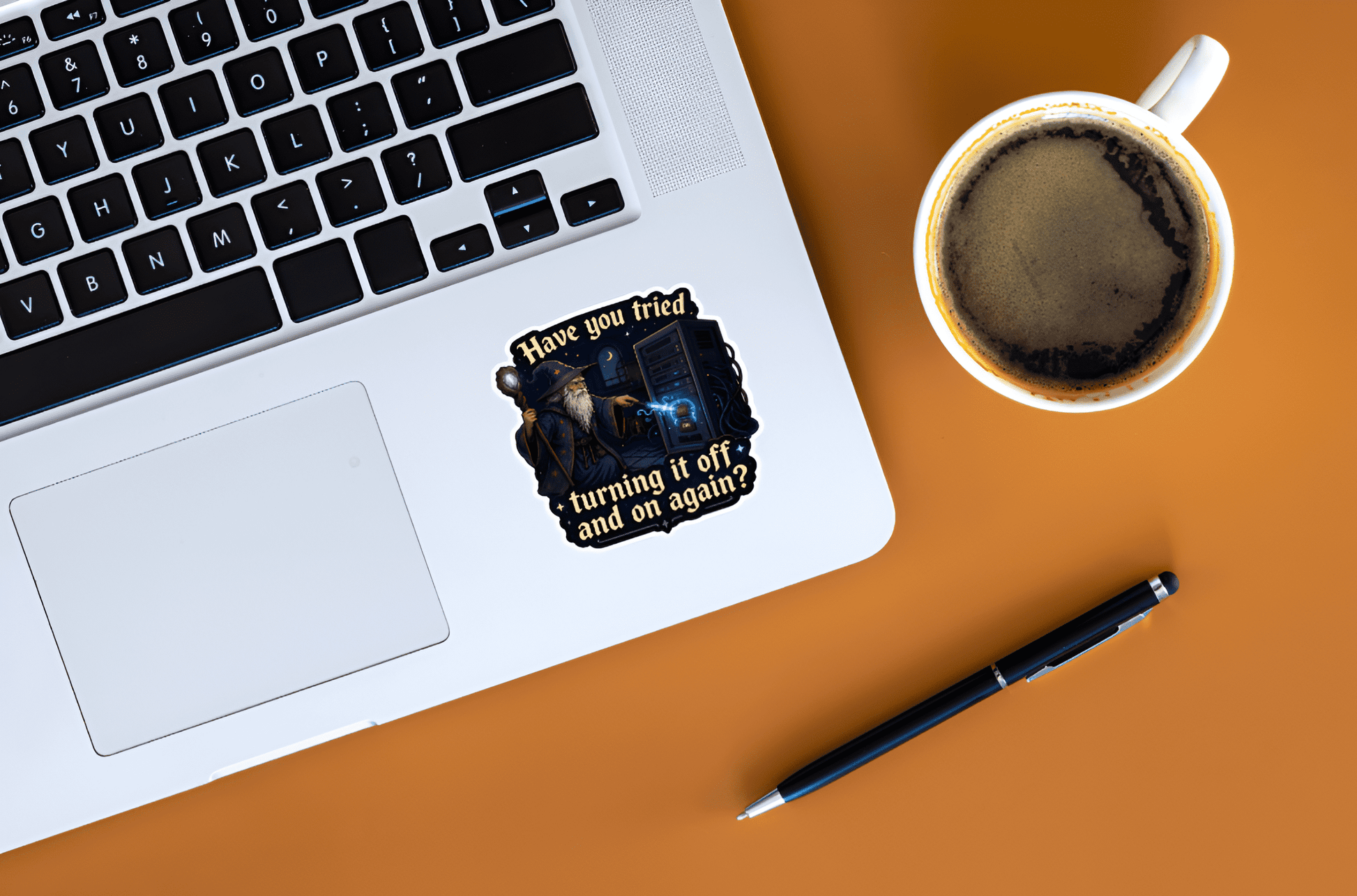 Laptop with a sticker on a brown surface next to a cup of coffee and pen