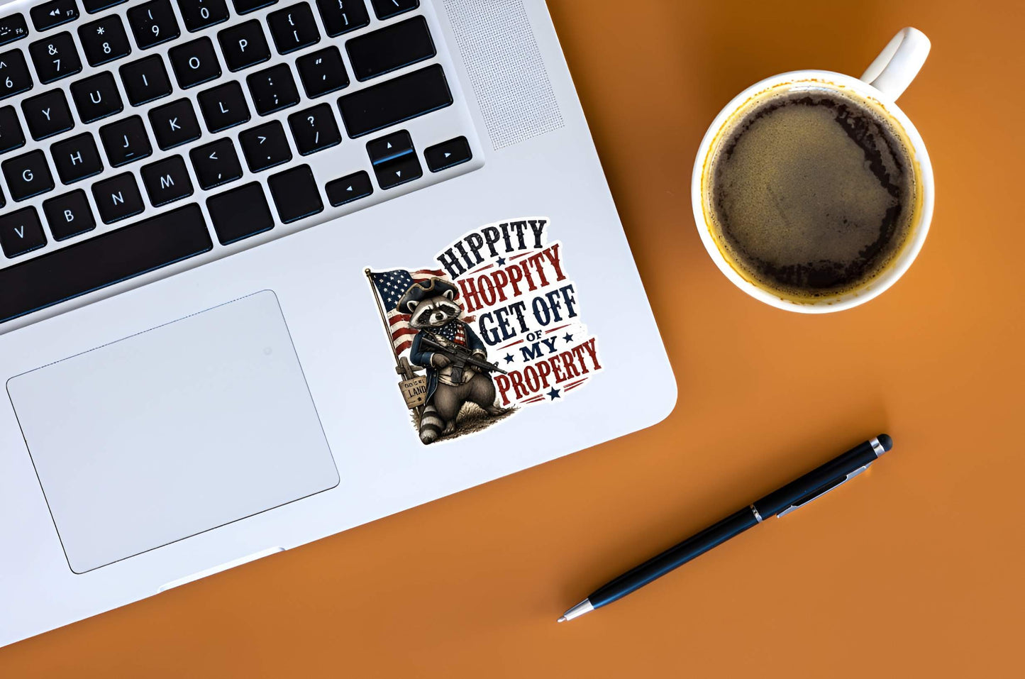 A flat, isolated vinyl sticker based on the file Hippity Hoppity with background.webp featuring a patriotic cartoon raccoon dressed as a colonial soldier holding a modern rifle, standing in front of an American flag and a "THIS IS MY LAND" wooden sign next to bold red and blue text reading "HIPPITY HOPPITY GET OFF OF MY PROPERTY".