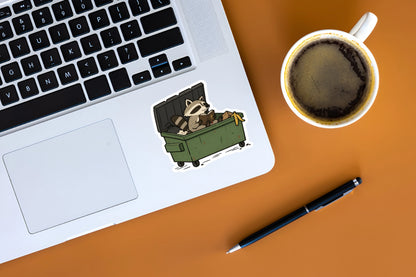 Funny Christian raccoon Bible sticker displayed on a silver laptop beside a cup of coffee