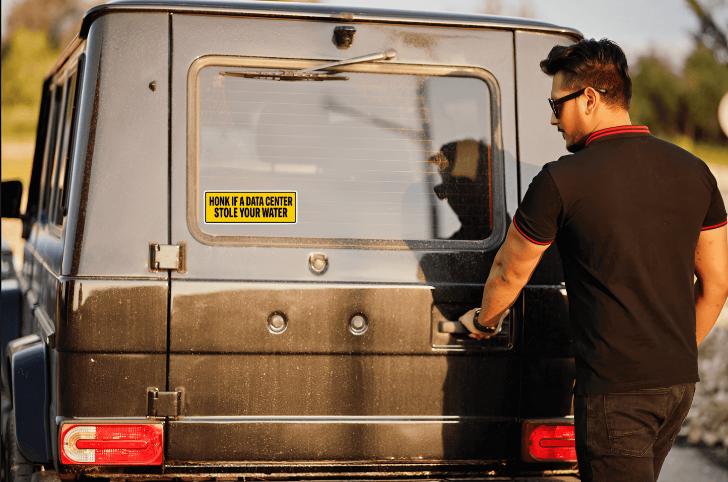 Person opening the door of a vehicle with a humorous sticker on the back window.
