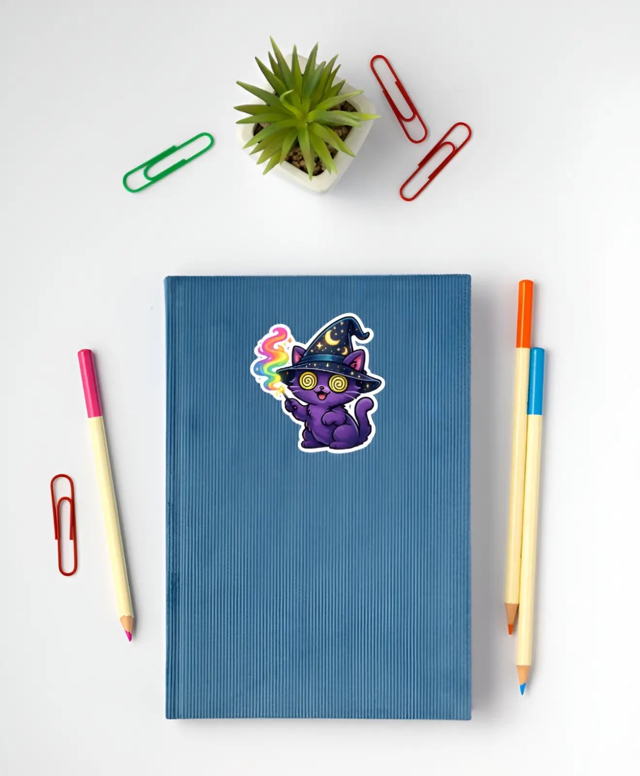 Blue notebook with a colorful cat sticker on a white background with stationery items.