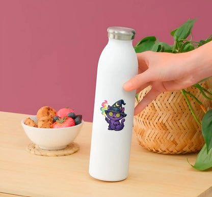 White water bottle with a colorful cat design held by a hand on a wooden table with a bowl of snacks and plant in the background.