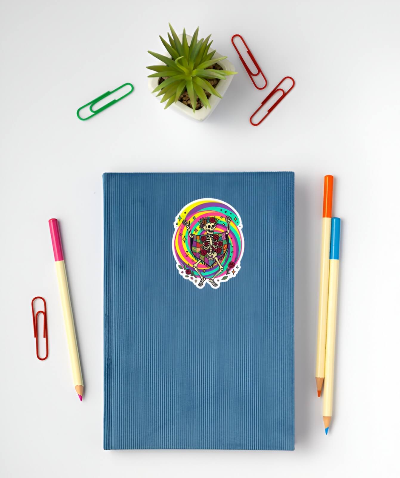 Blue notebook with a colorful sticker on a white surface with stationery items.