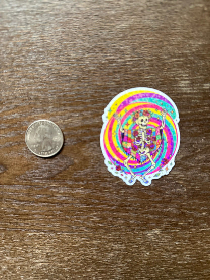 Colorful sticker with a skeleton design next to a quarter on a wooden surface