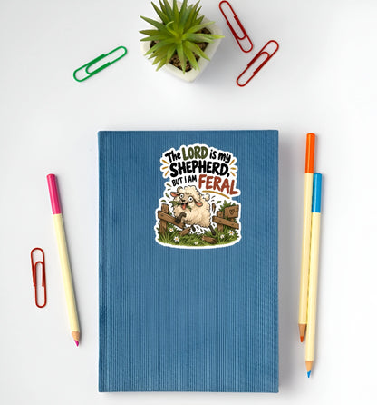 A blue ribbed hardcover notebook with a cartoon sheep sticker on the front, styled in a flat lay with pens, paperclips, and a small potted succulent on a white background.