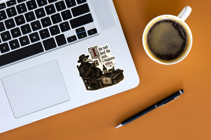 I Diagnose Vibes plague doctor sticker displayed on a silver laptop beside a cup of coffee