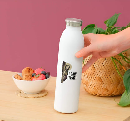 White water bottle withf a Jesus Christ with 'I Saw That!' text held by a hand on a wooden table with a bowl of snacks and plant in the background.
