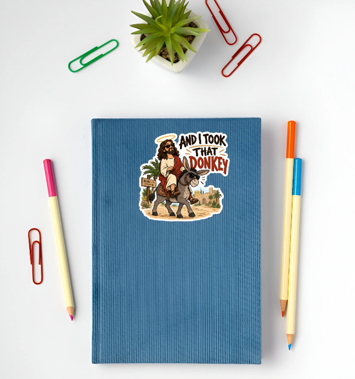And I Took That Donkey funny Jesus sticker displayed on a blue notebook