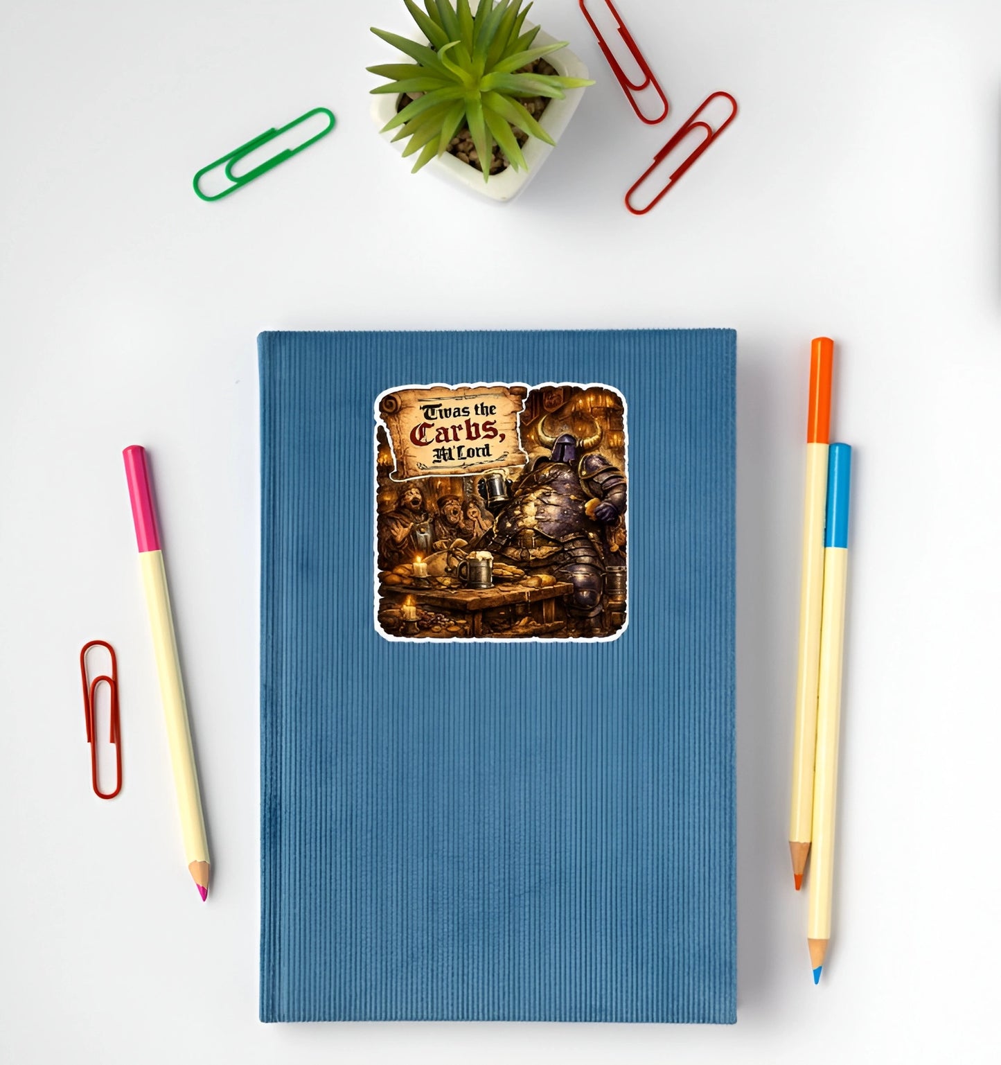 Funny Twas the Carbs M’Lord medieval knight sticker displayed on a blue notebook