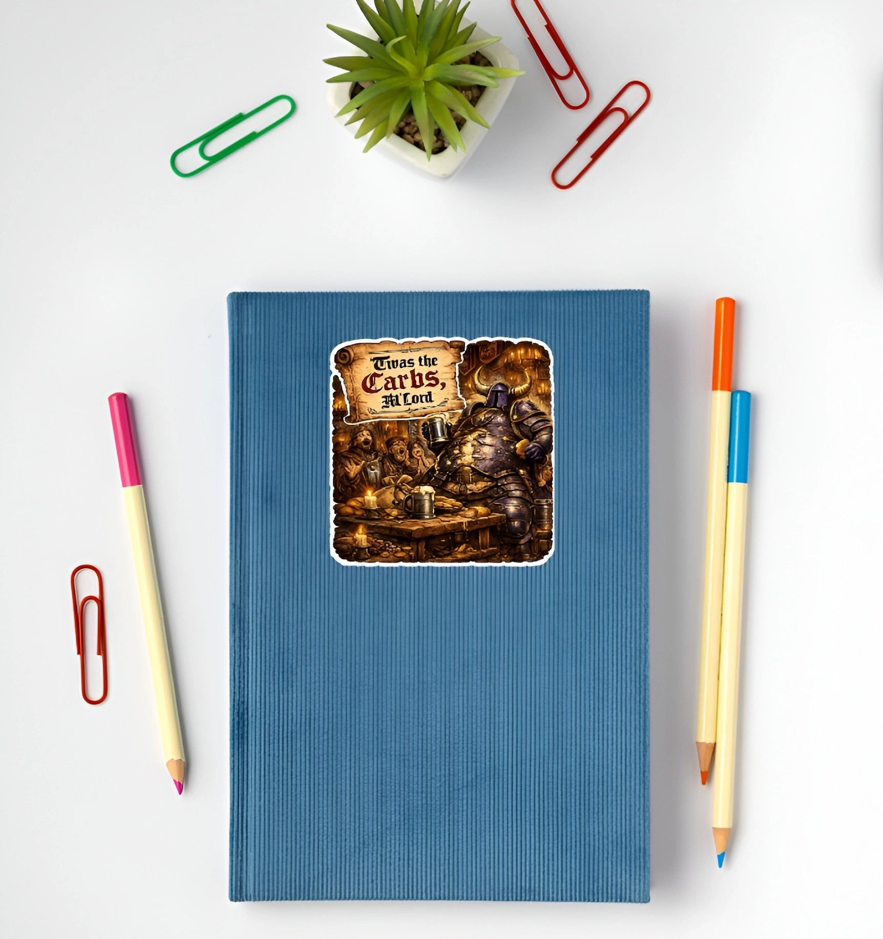 Funny Twas the Carbs M’Lord medieval knight sticker displayed on a blue notebook