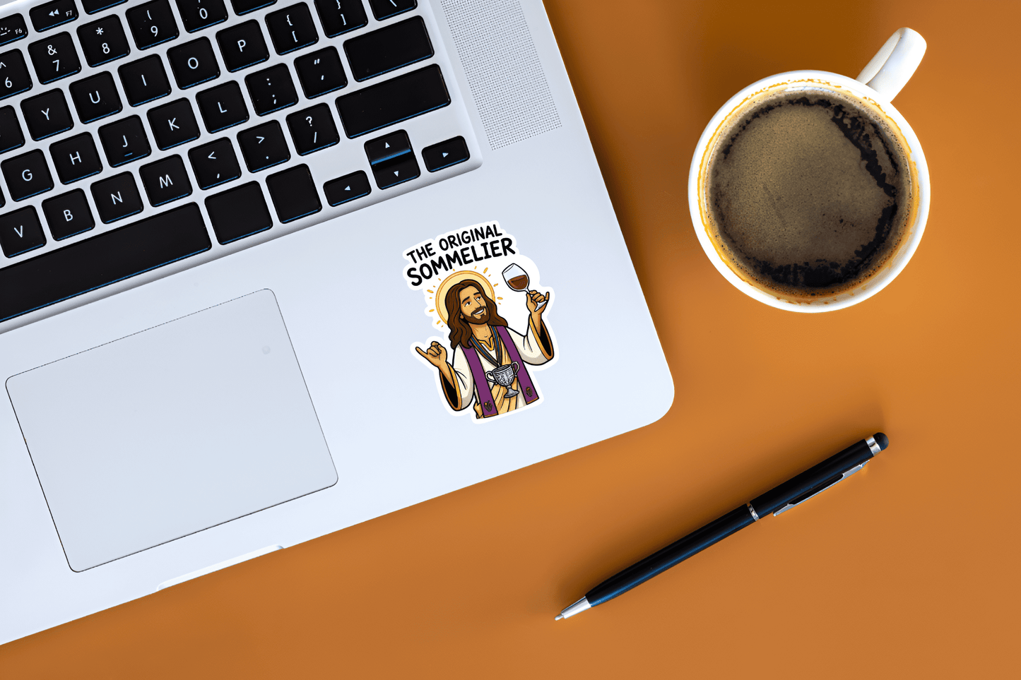 Laptop with a 'The Original Sommelier' sticker, coffee cup, and pen on an orange surface
