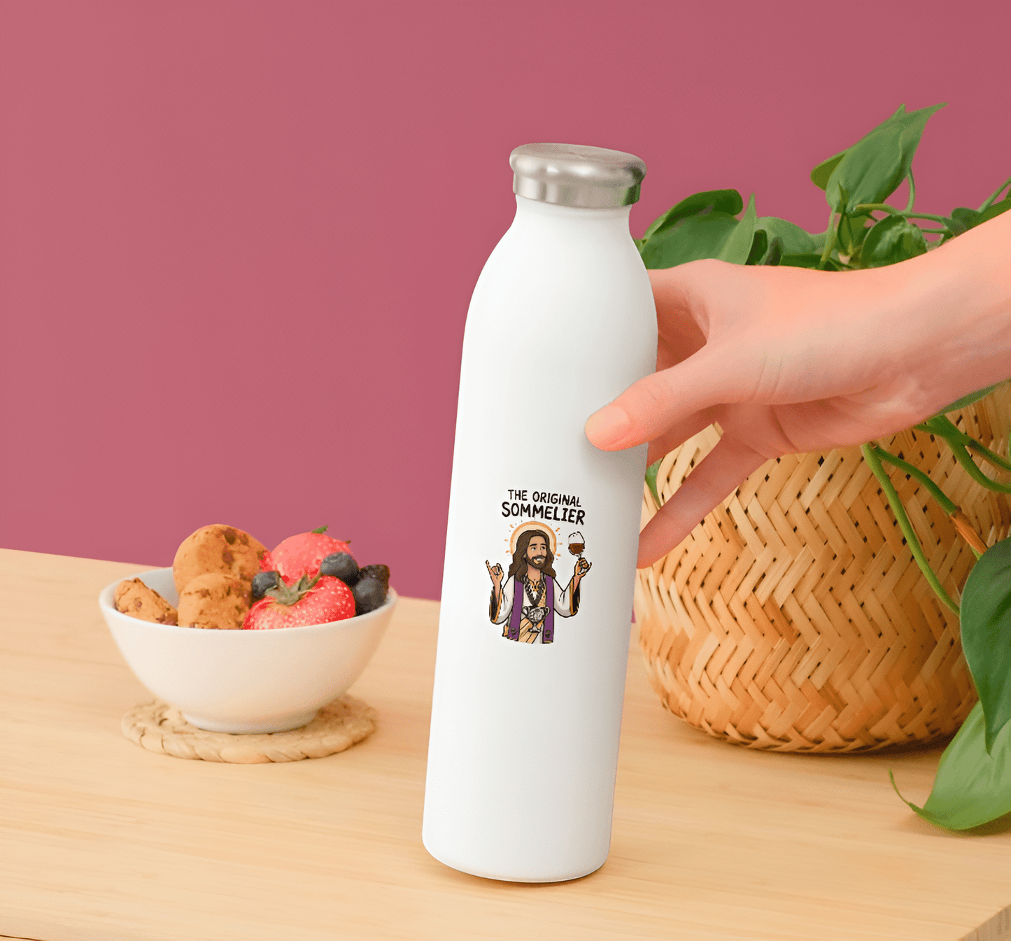 White water bottle with a graphic design on a wooden table with a bowl of fruit and a plant in the background.