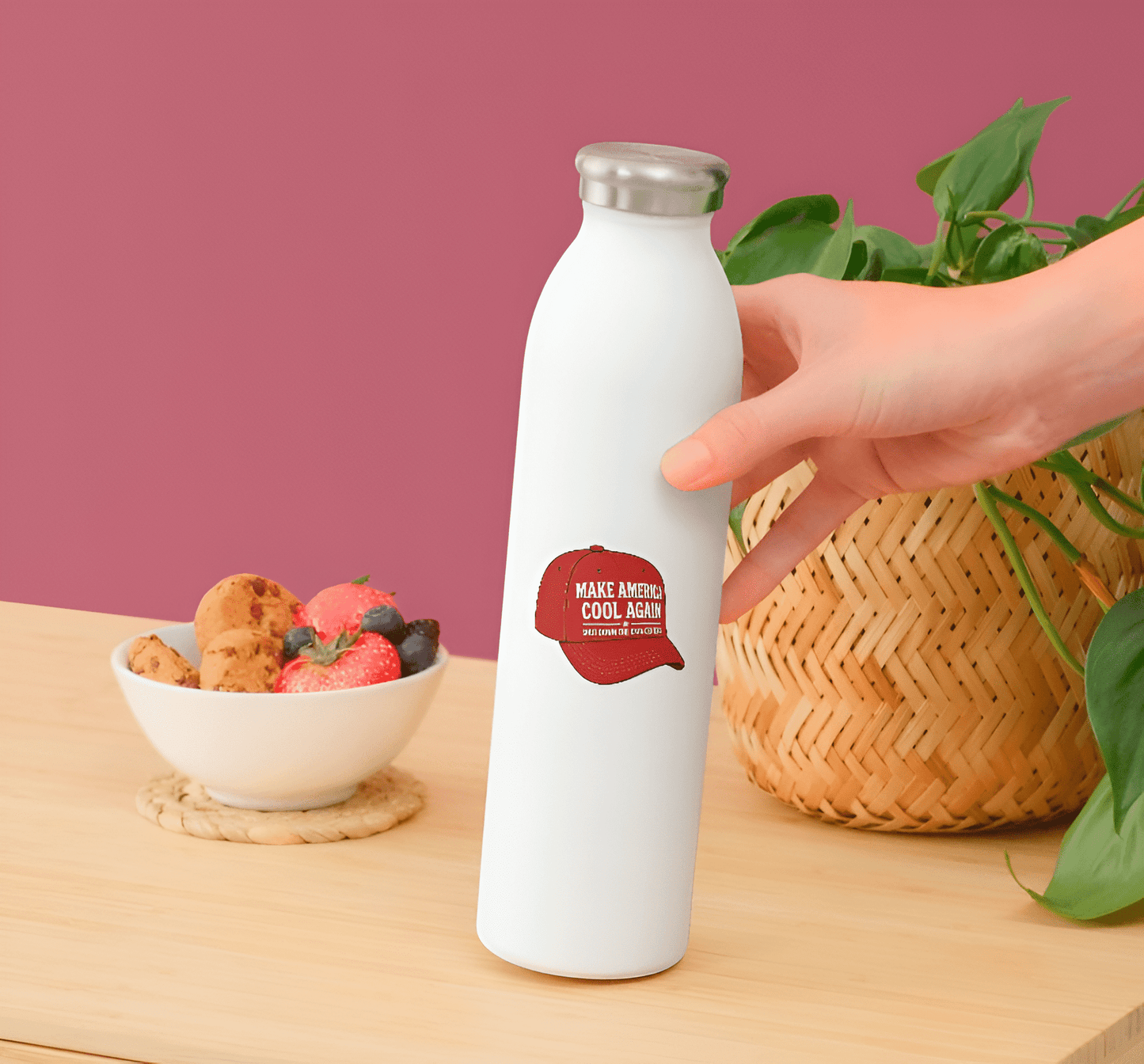 White water bottle with red label held by a hand on a wooden table with snacks and a plant.