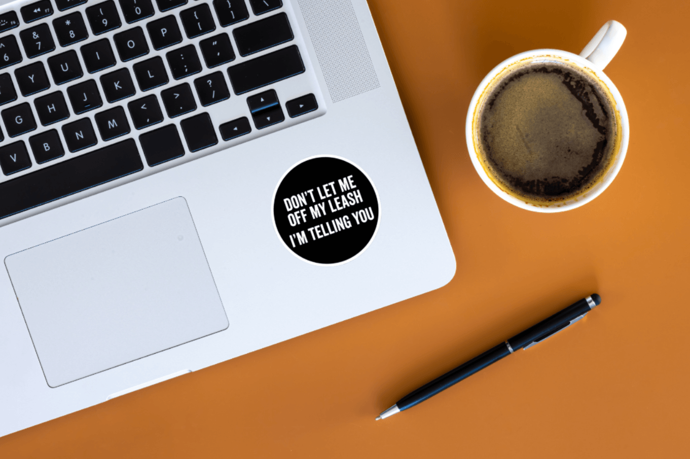 Laptop with a sticker on a desk next to a cup of coffee and pen
