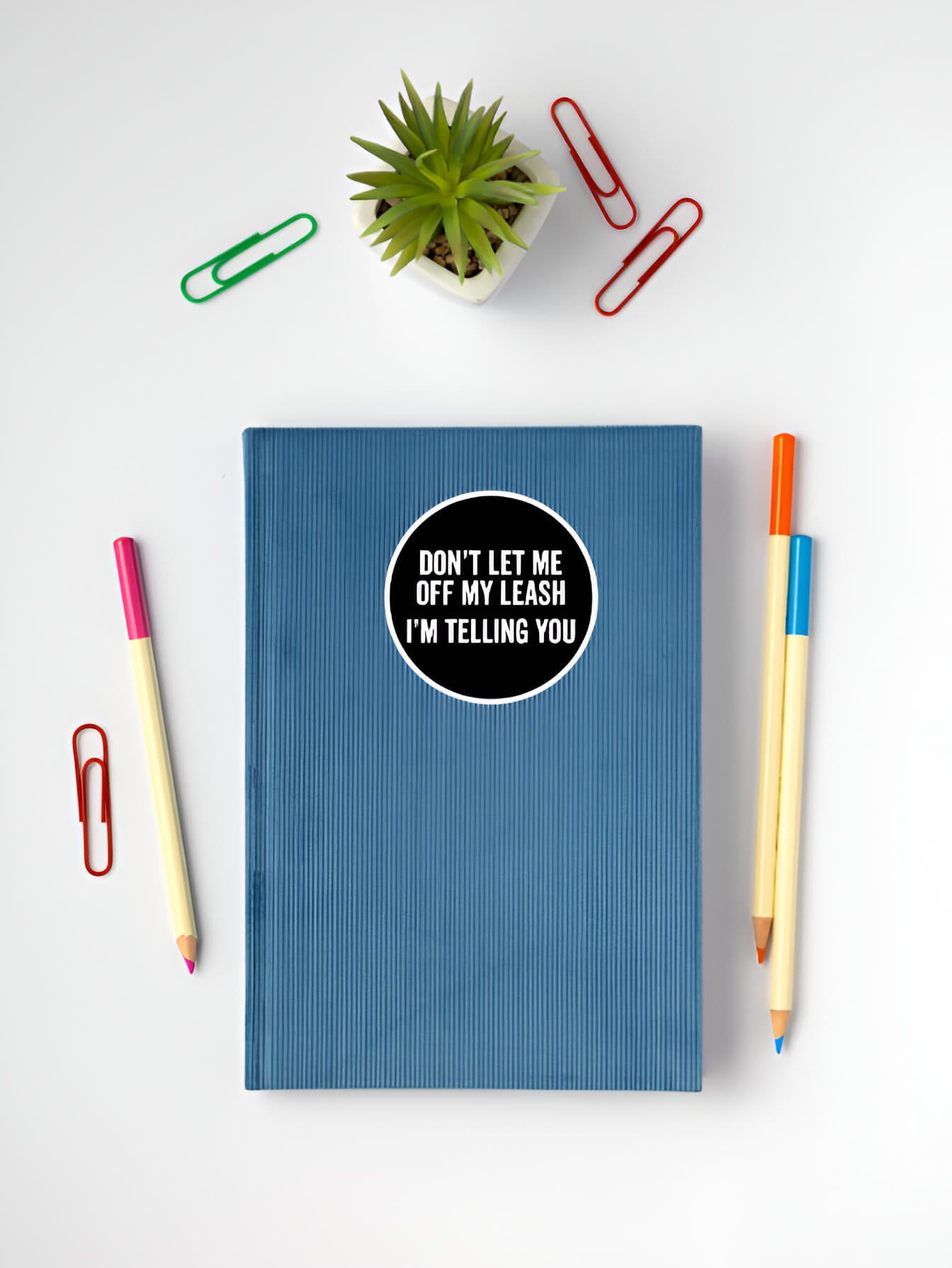 Blue notebook with a sticker on a white surface with stationery items