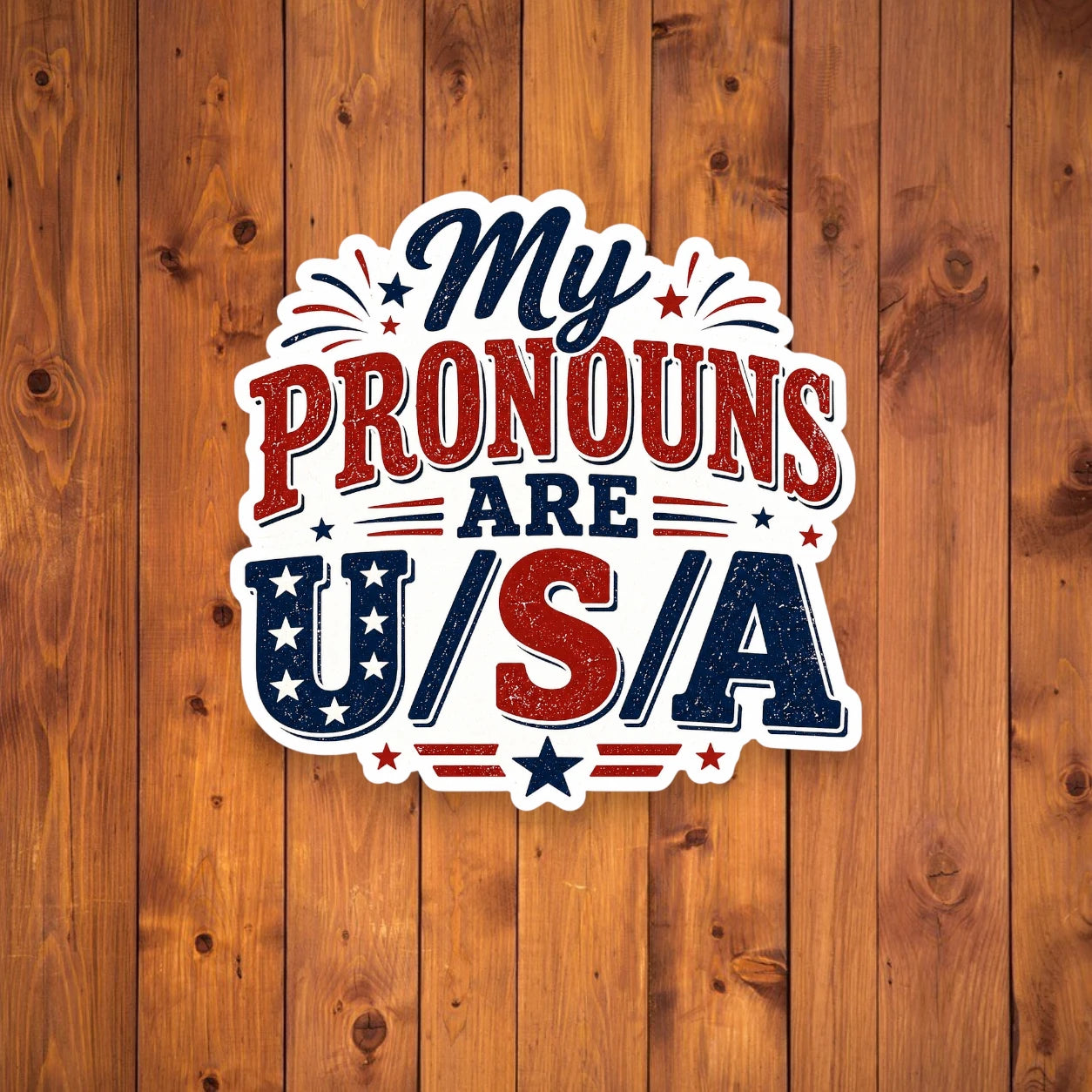 Sticker with 'My Pronouns Are U/S/A' text on a wooden background
