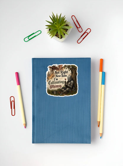 Funny knight sticker reading Not Right Now Babe I’m Cultivating Whimsy on a blue notebook