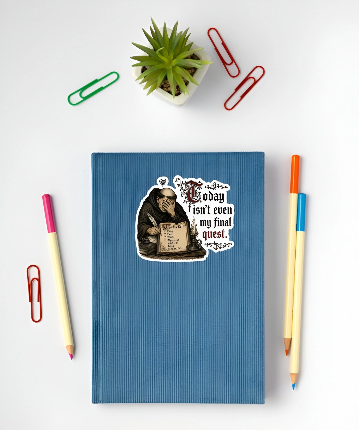 A blue hardcover notebook with a humorous sticker of a monk reading and the text 'I don't know, isn't even my final quest. 