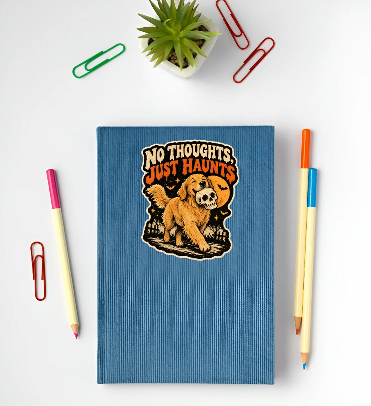 No Thoughts Just Haunts golden retriever Halloween sticker with skull displayed on a blue notebook