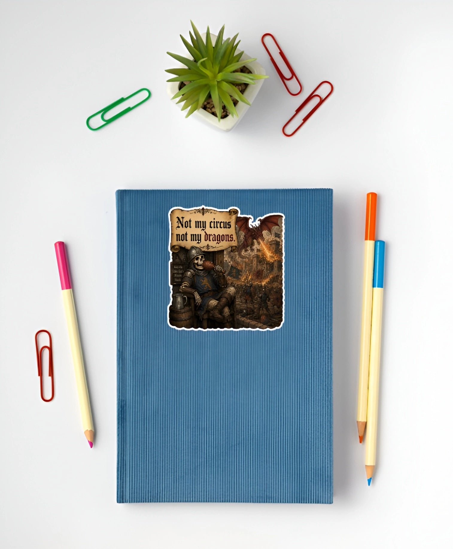 Medieval dragon meme sticker reading Not My Circus Not My Dragons on a blue notebook