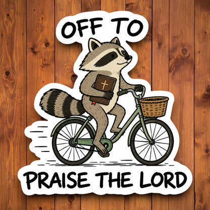 Off to Praise the Lord funny raccoon bicycle sticker shown on a wood background