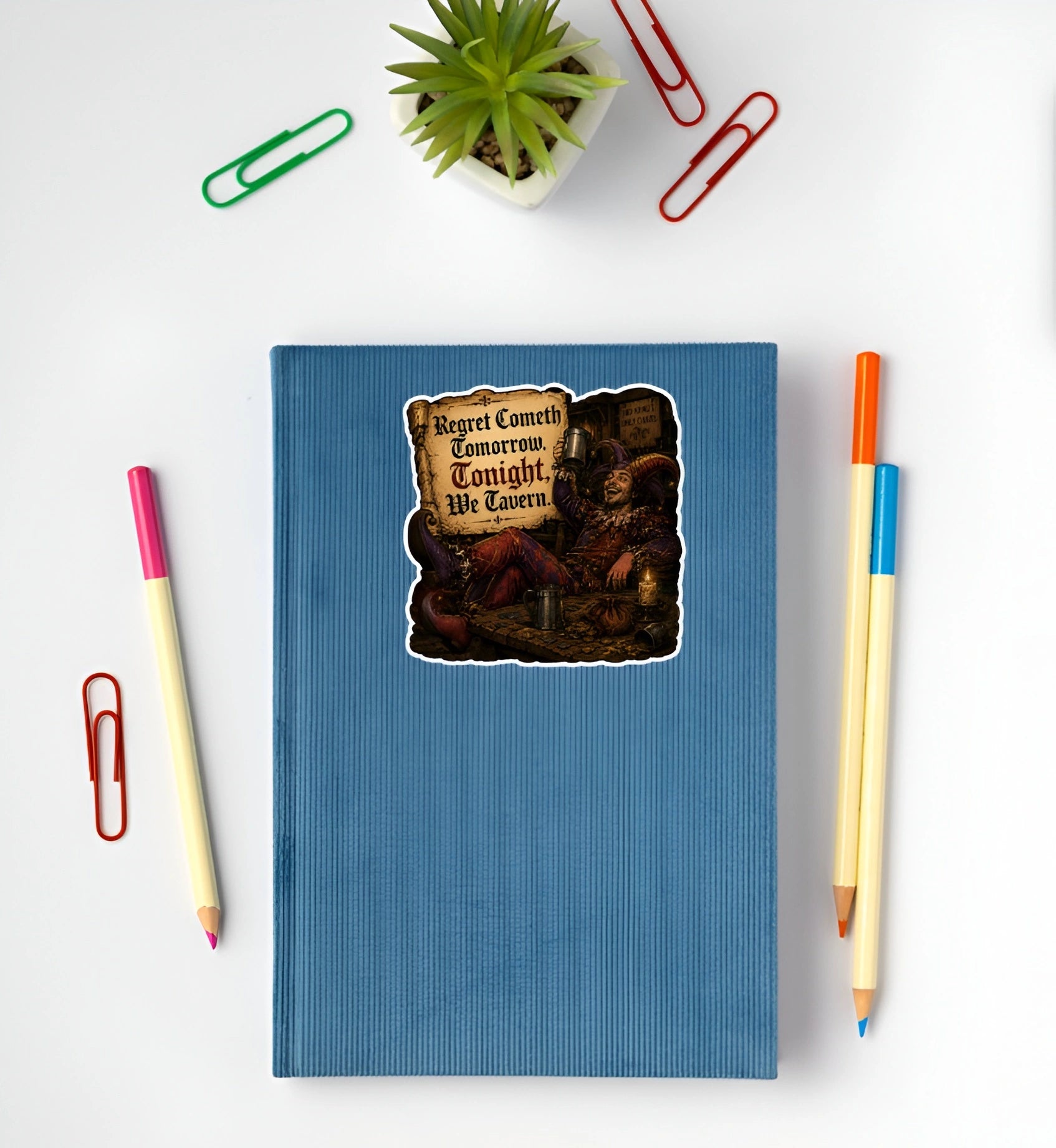 Funny medieval jester sticker reading Regret Cometh Tomorrow Tonight We Tavern displayed on a blue notebook
