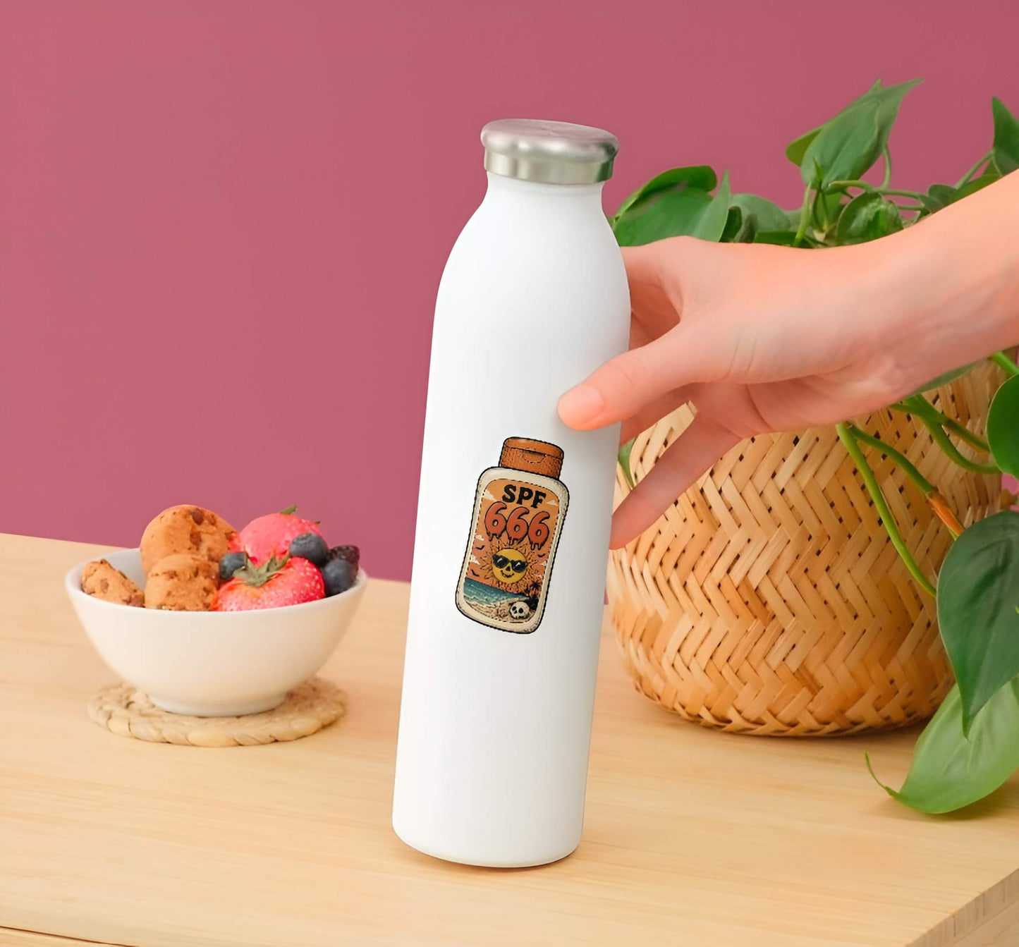 White water bottle with a custom label held by a hand on a wooden table with a bowl of fruit and a plant.