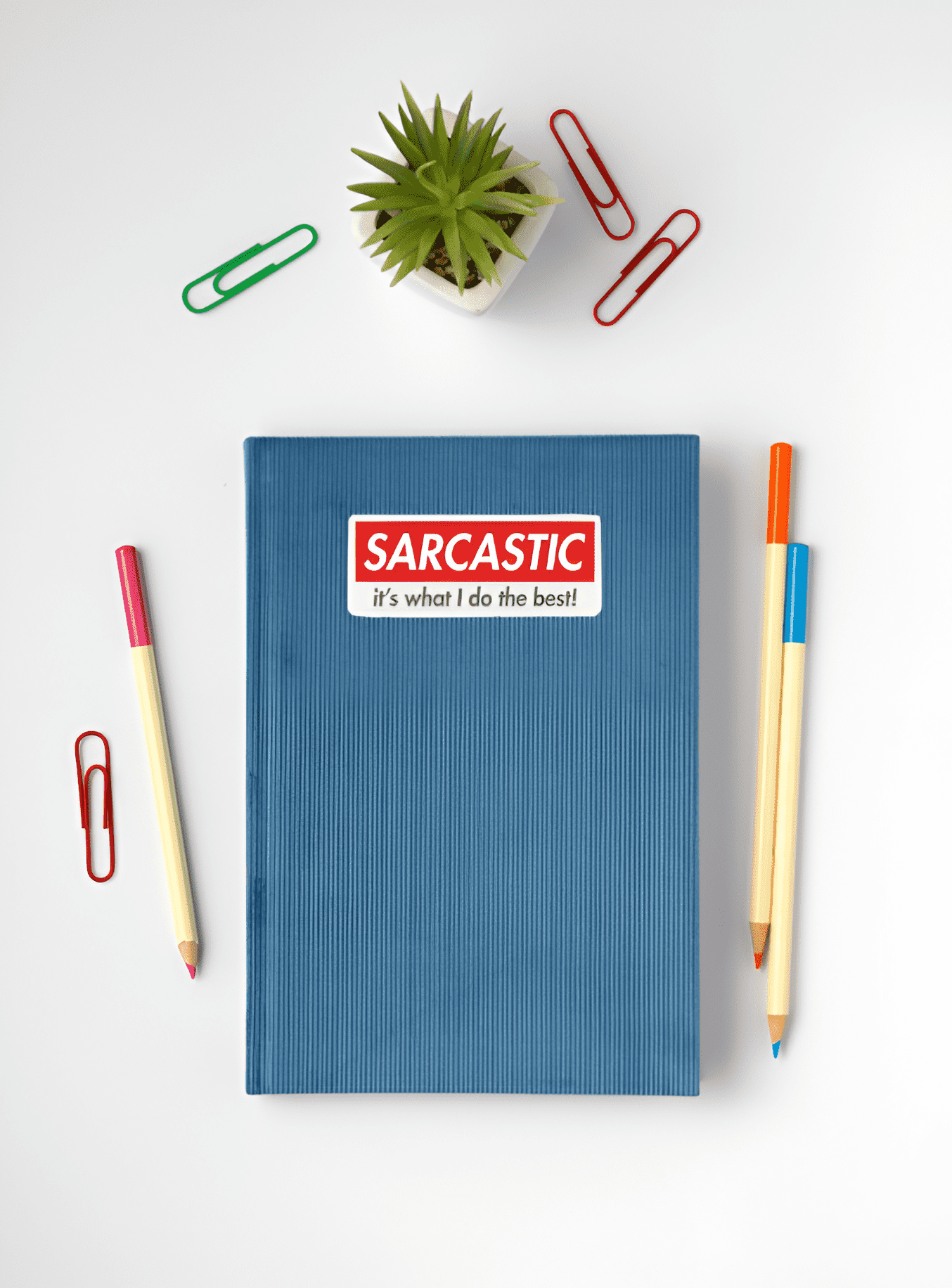 Blue notebook with a 'Sarcastic' sticker, surrounded by stationery items on a white background