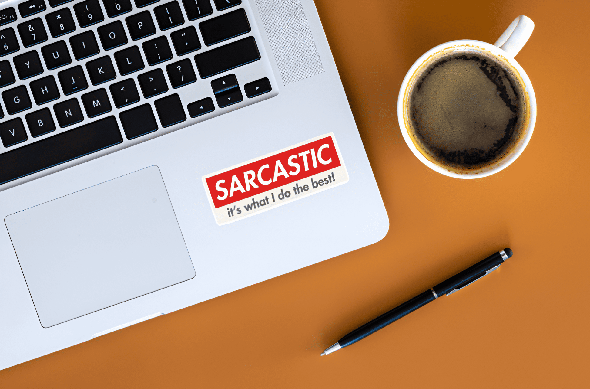 Laptop with a 'Sarcastic' sticker, coffee cup, and pen on a brown surface