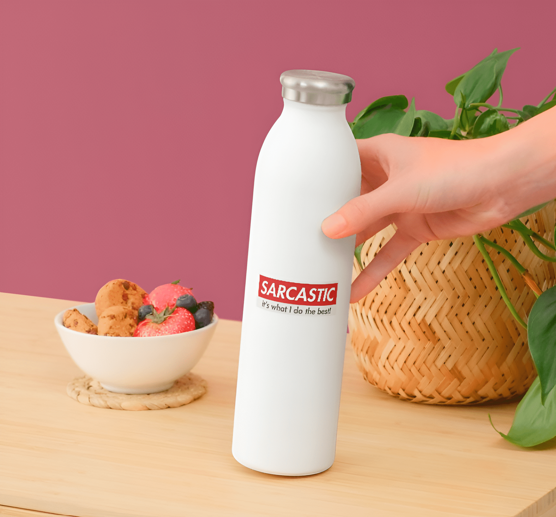 White water bottle with 'Sarcastic' text on a wooden table with a bowl of snacks and plant in the background.