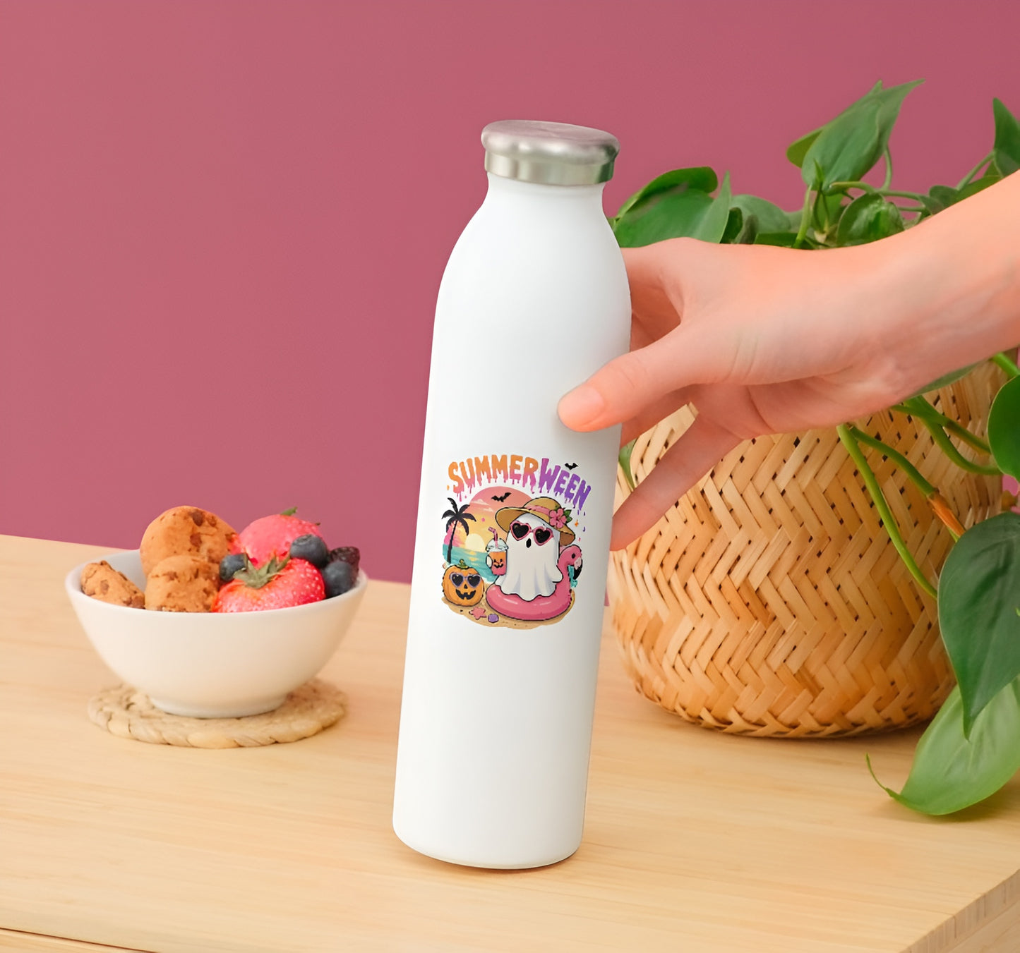 White water bottle with a summer-themed design held by a hand on a wooden surface with a bowl of snacks and plant in the background.