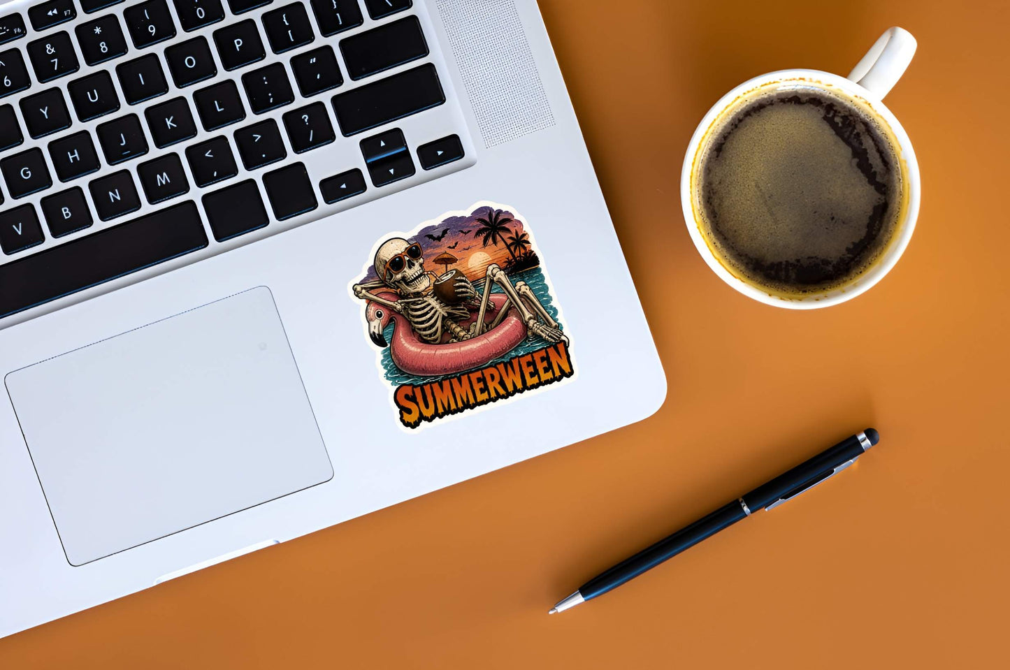 Laptop with a 'Summerween' sticker, coffee cup, and pen on an orange surface