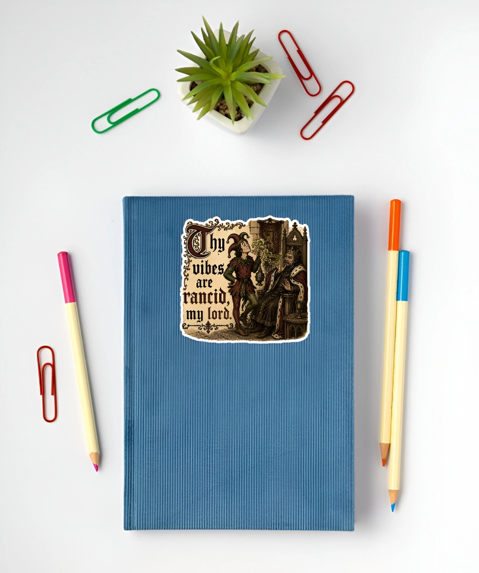 Thy Vibes Are Rancid My Lord medieval meme sticker displayed on a blue notebook