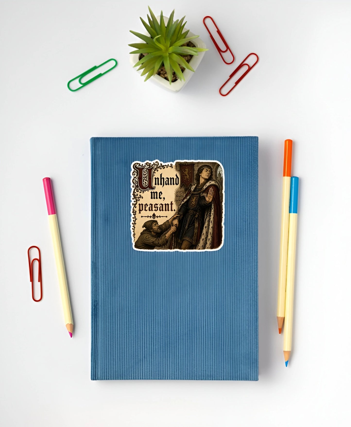 Unhand Me Peasant sticker displayed on a blue notebook