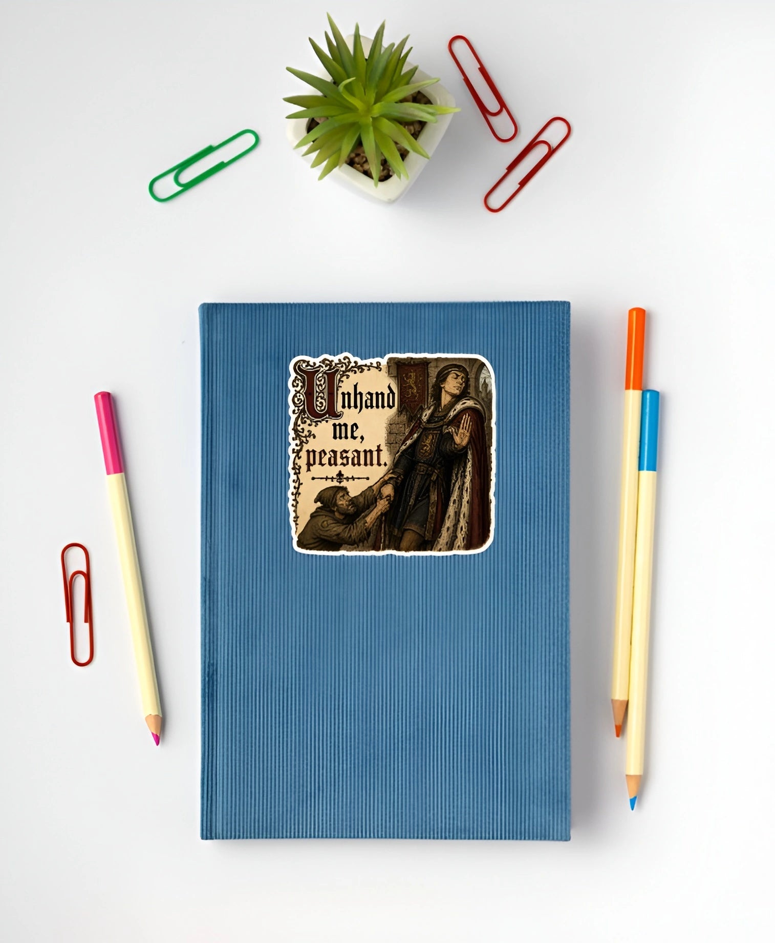 Unhand Me Peasant sticker displayed on a blue notebook