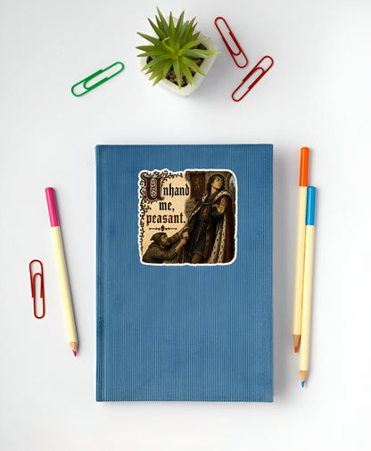 Unhand Me Peasant sticker displayed on a blue notebook