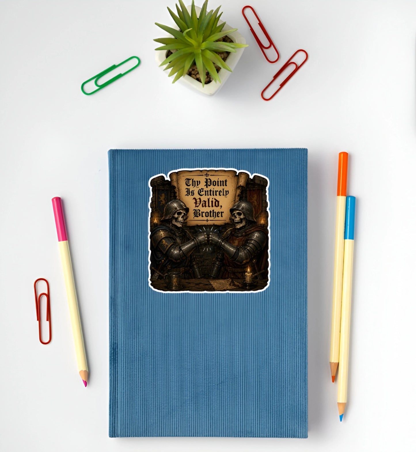 Thy Point Is Entirely Valid Brother medieval skeleton knight sticker displayed on a blue notebook