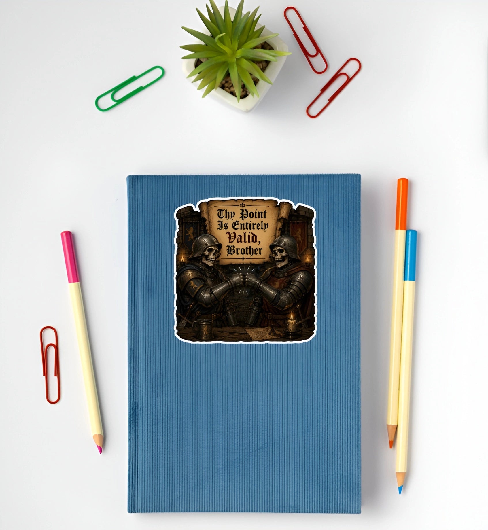 Thy Point Is Entirely Valid Brother medieval skeleton knight sticker displayed on a blue notebook
