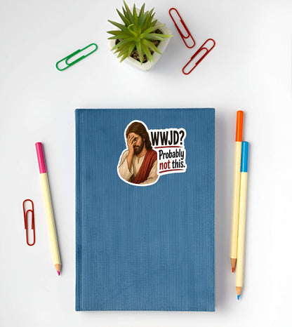 Blue notebook with a Jesus wearing cream and red robes, holding his hand over his face in an exhausted facepalm gesture next to bold text reading "WWJD? Probably not this."sticker of a cartoon character and text, surrounded by pens and paper clips on a white background.
