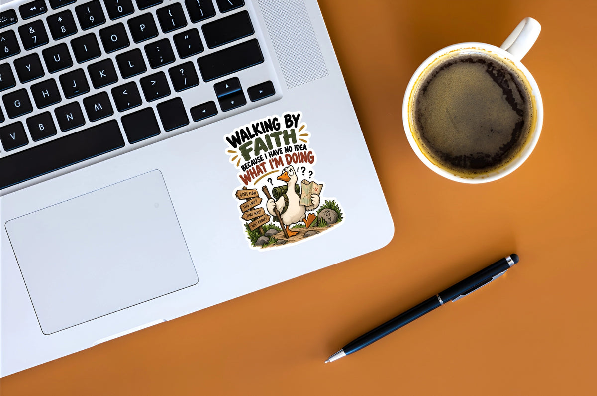 A die-cut vinyl sticker with a cartoon illustration and the text 'WALKING BY FAITH WHAT I'M DOING?' is shown on the palm rest of a silver laptop. The scene is styled as a flat-lay on an orange surface, alongside a cup of coffee, a black pen, and part of a laptop keyboard.
