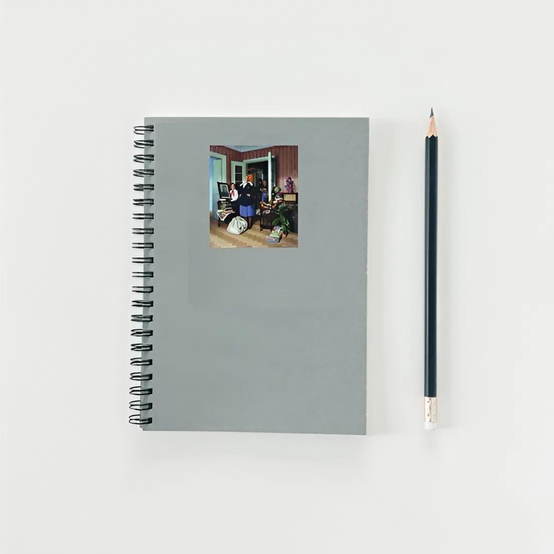 Gray spiral-bound notebook with a photo on the cover and a black pencil next to it on a light gray background