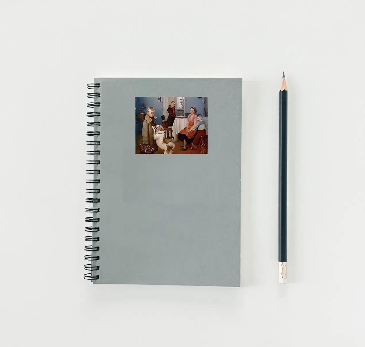 Gray spiral-bound notebook with a printed cover image of two people and a dog, next to a black pencil on a light gray background.